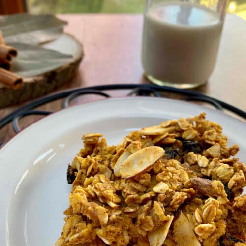 A pumpkin spiced oat bar on a white plate with a glass of milk in the background.