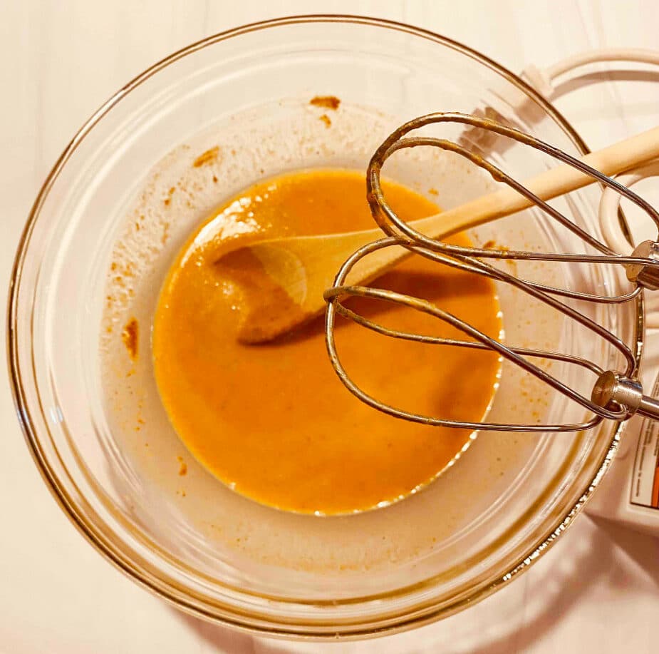 A glass bowl on a marble counter with pumpkin puree, almond milk, almond butter, an egg and maple syrup combined.