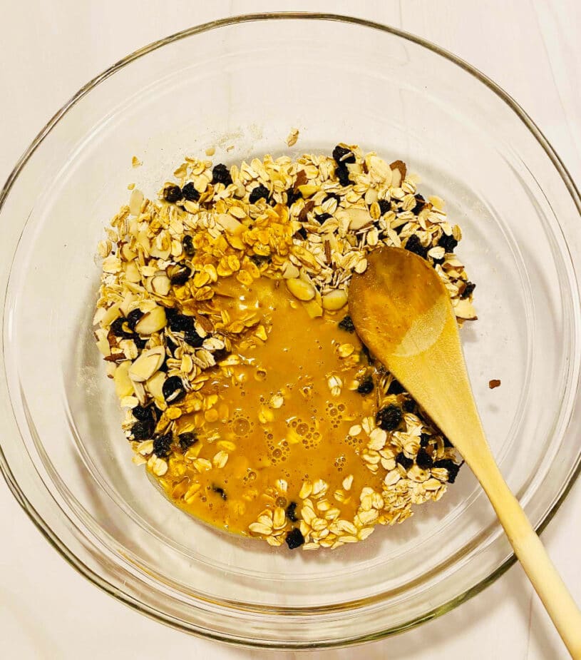A glass bowl with liquid pumpkin and almond milk mix on top of the oats with almonds and raisins.