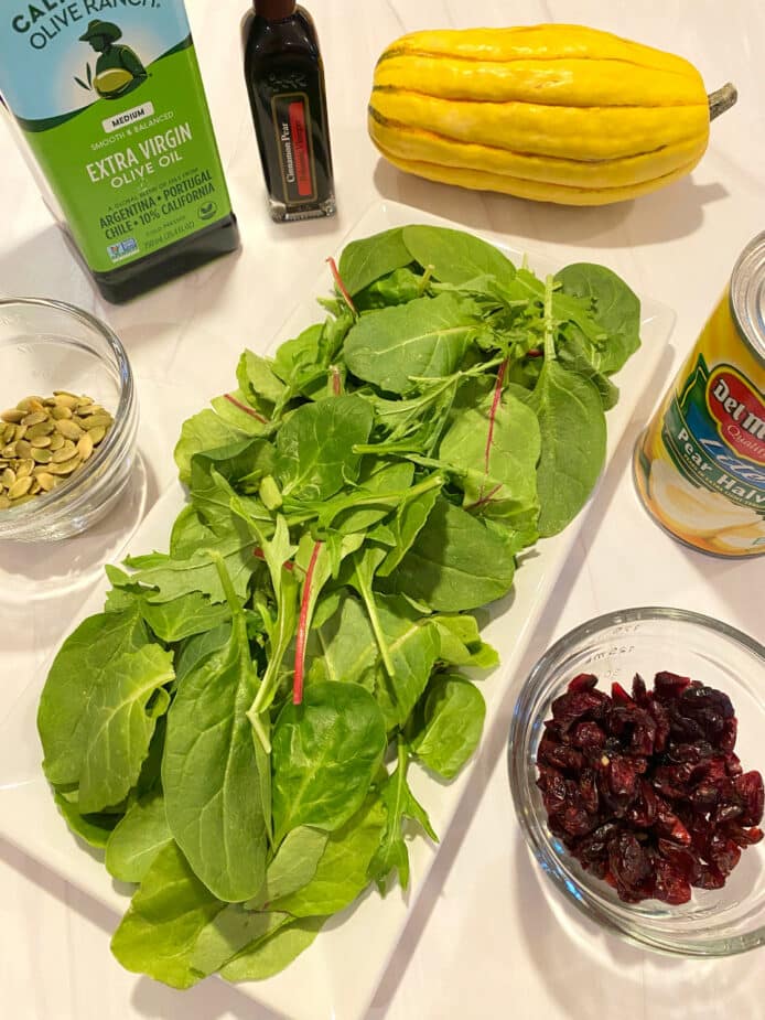 A platter of power greens surrounded by squash, pears, cranberries and pumpkin seeds used to make the salad sitting on a white counter