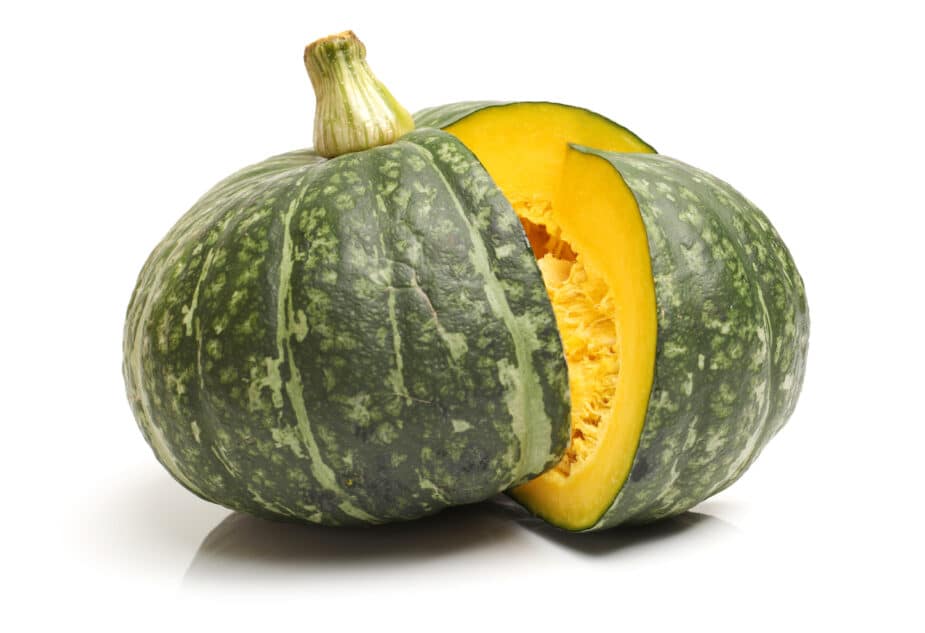 A green speckled Kabocha squash that is cut open showing its orange interior.