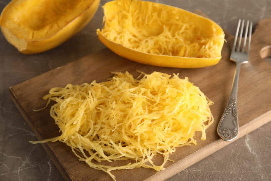 Cooked spaghetti squash scooped out of its shell on a wooden cutting board