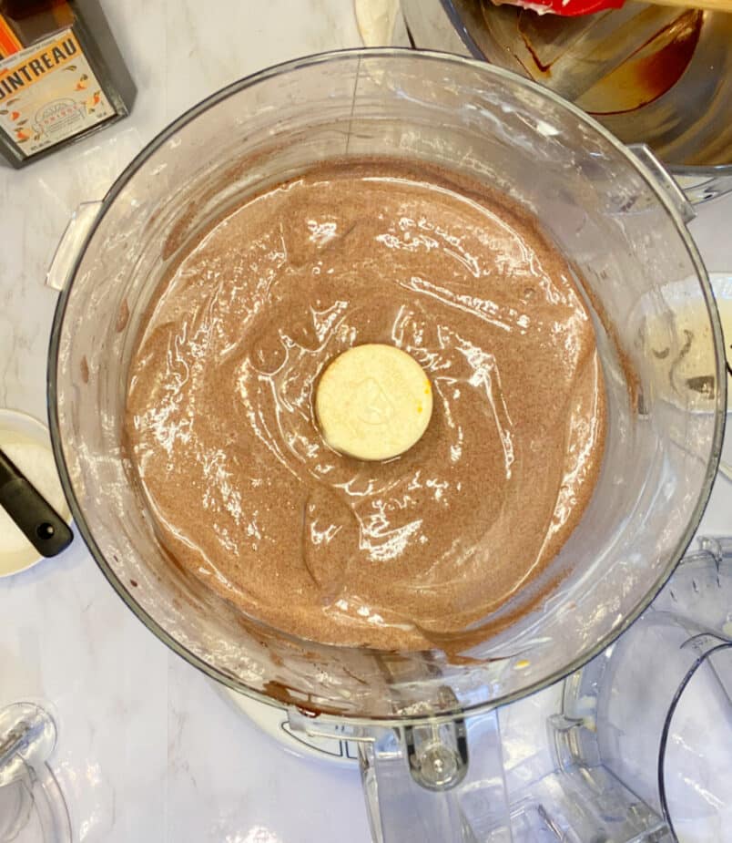 A food processor sitting on a marble counter with dark chocolate orange mousse inside the processor.