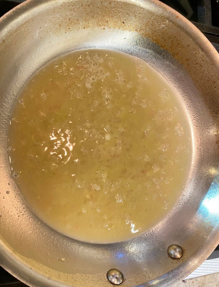 A frying pan on a stove with white wine, lemon juice and shallots that has been reduced to a thick, syrupy sauce