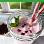 A pink smoothie in a glass cup with colorful straws. Pomegranate seeds and mint garnish the top.