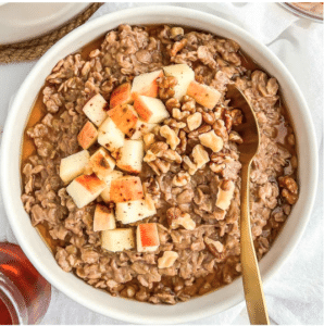 A bowl of oatmeal seasoned with cinnamon and topped with chopped apples on a white background