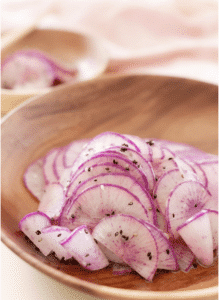 A bowl of sliced purple daikon radishes with black sesame seeds