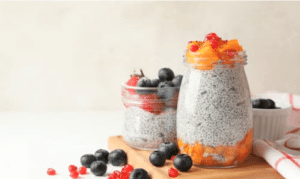 Clear glass jars with kefir chia pudding and berries on a white background.