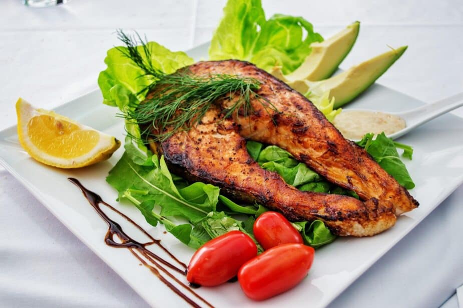 A grilled salmon steak on a bed of lettuce with tomatoes and avocado on the side.