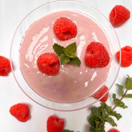 Raspberry Silken Tofu Mousse in a glass cup garnished with fresh raspberries and mint on a white counter.