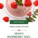 A glass dish filled with raspberry tofu mousse with fresh raspberries and a sprig of fresh mint on a white counter.