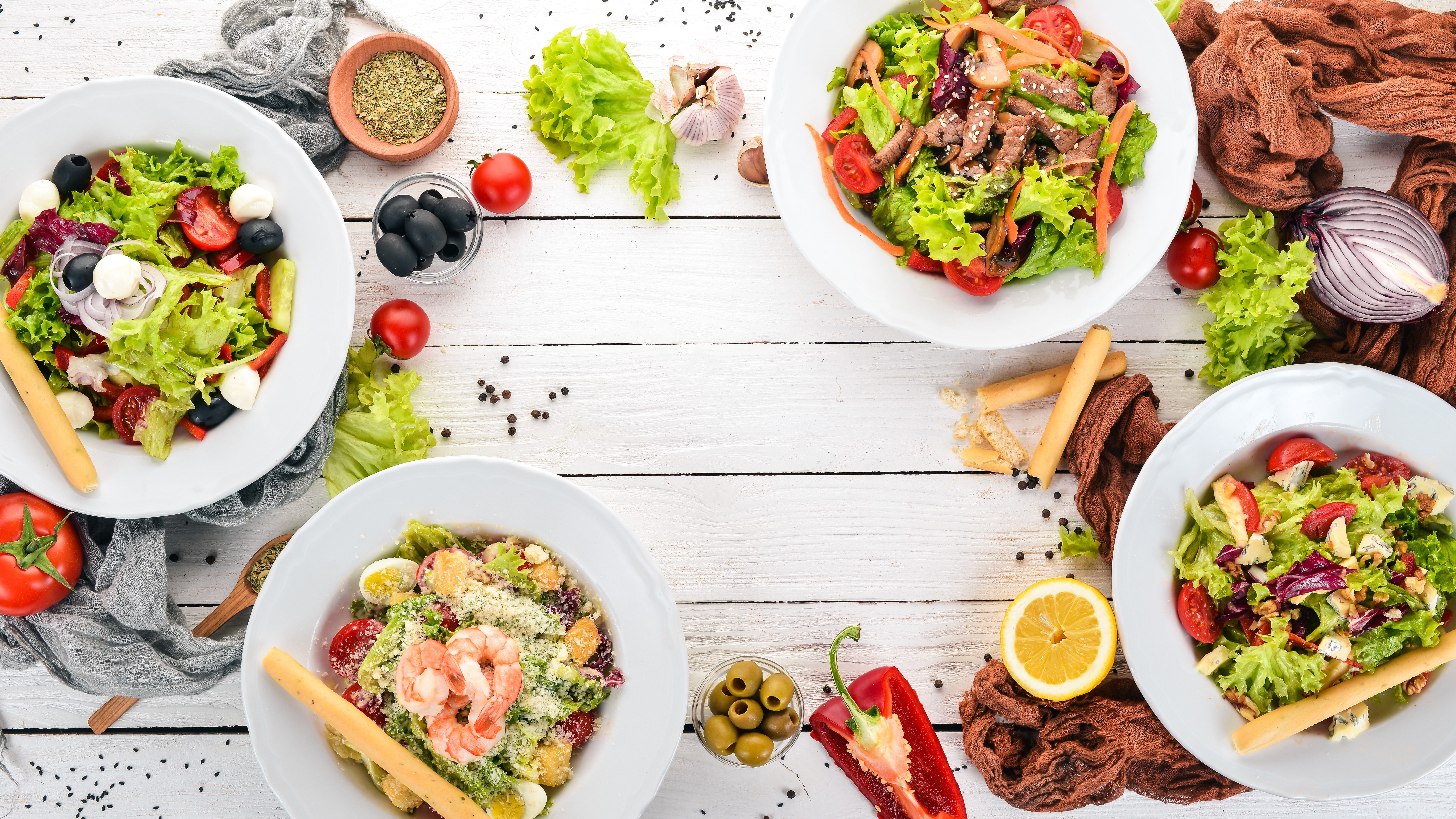 A white wood picnic table with salad bowls and healthy ingredients surrounding them.  