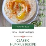 A picture of hummus in a white bowl on a picnic table. The title "Classic Hummus recipe with garlic and lemon" is below