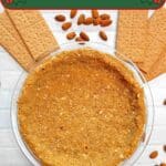 A graham cracker pie crust in a glass pie pan surrounded by graham crackers and almonds.