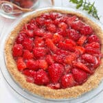 A strawberry pie on a white picnic table with a clear bowl of fresh strawberries in the background