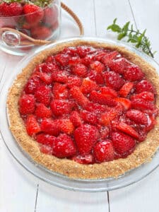 A strawberry pie on a white picnic table with a clear bowl of fresh strawberries in the background