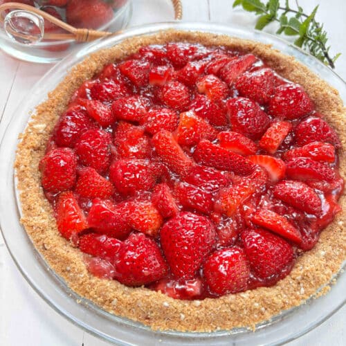 A strawberry pie on a white picnic table with a clear bowl of fresh strawberries in the background