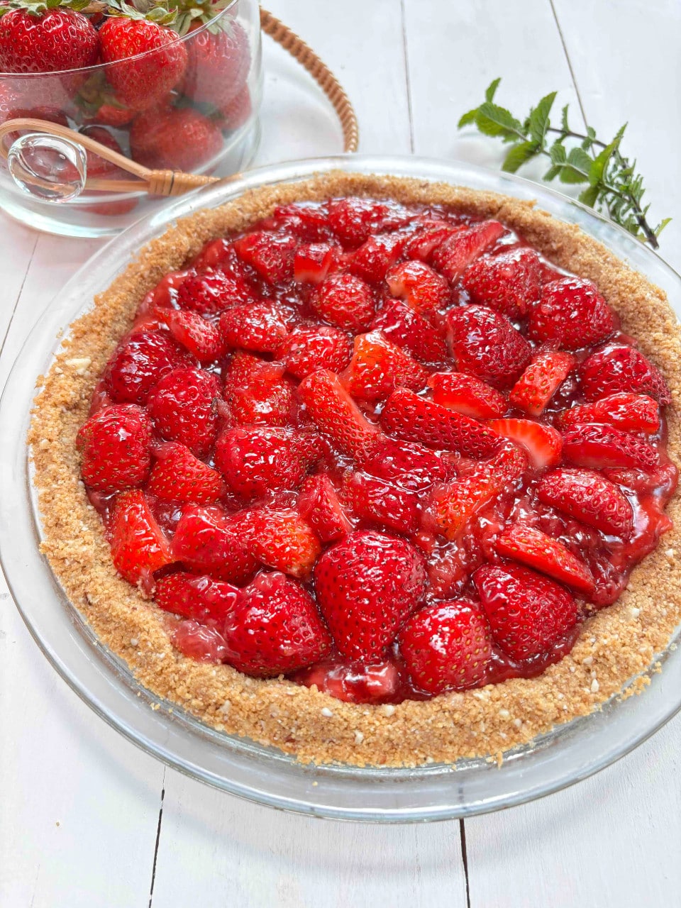 A strawberry pie on a white picnic table with a clear bowl of fresh strawberries in the background