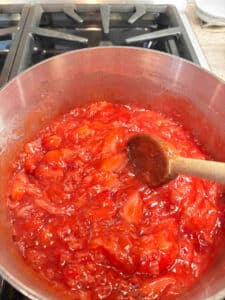 The strawberry filling after cooking and thickened in a saucepan. The strawberry filling is a bright clear red color with pieces of strawberries throughout.