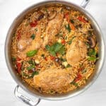 A sautepan filled with orzo, sundried tomatoes, mushrooms and chicken breasts on a marble counter