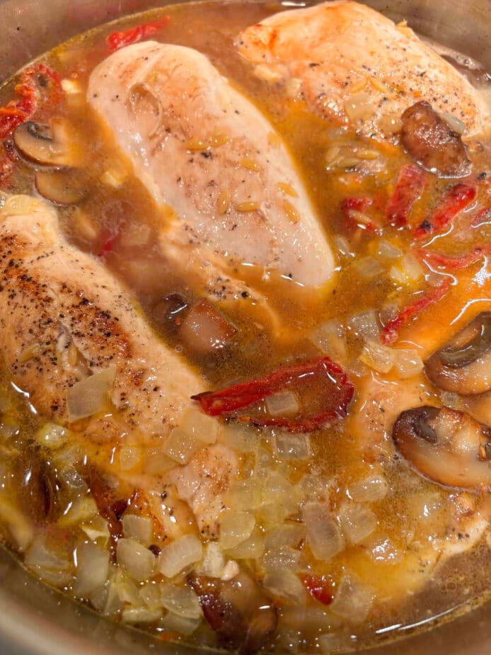 Chicken breasts submerged in broth with sundried tomatoes, onions, orzo, and mushrooms 