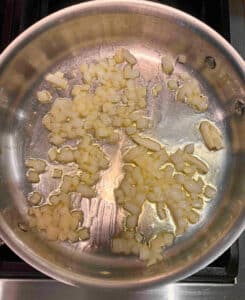 Onions in olive oil cooking in a metal sautepan on the stove