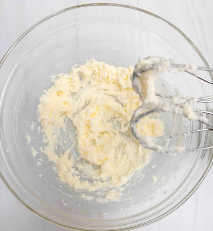 Butter and sugar creamed in a glass bowl with the beaters over the bowl. The bowl is on a marble counter