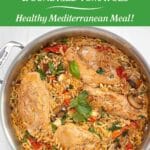 A saute pan filled with cooked orzo, chicken breasts, sundried tomatoes, mushrooms and spinach garnished with fresh basil and pine nuts. It is sitting on a marble counter.