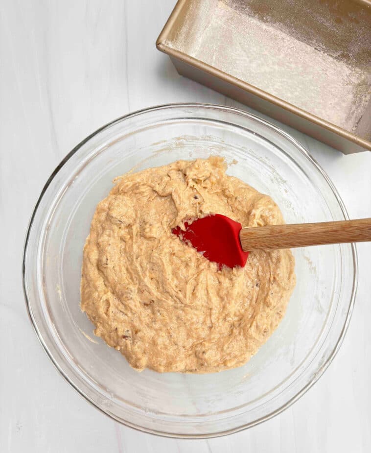 Banana Bread Batter in a glass bowl ready to be poured into the loaf pan. A red spatula is in the batter