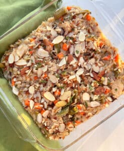 A glass casserole dish filled with salmon and brown and wild rice and vegetables, topped with sliced almonds.