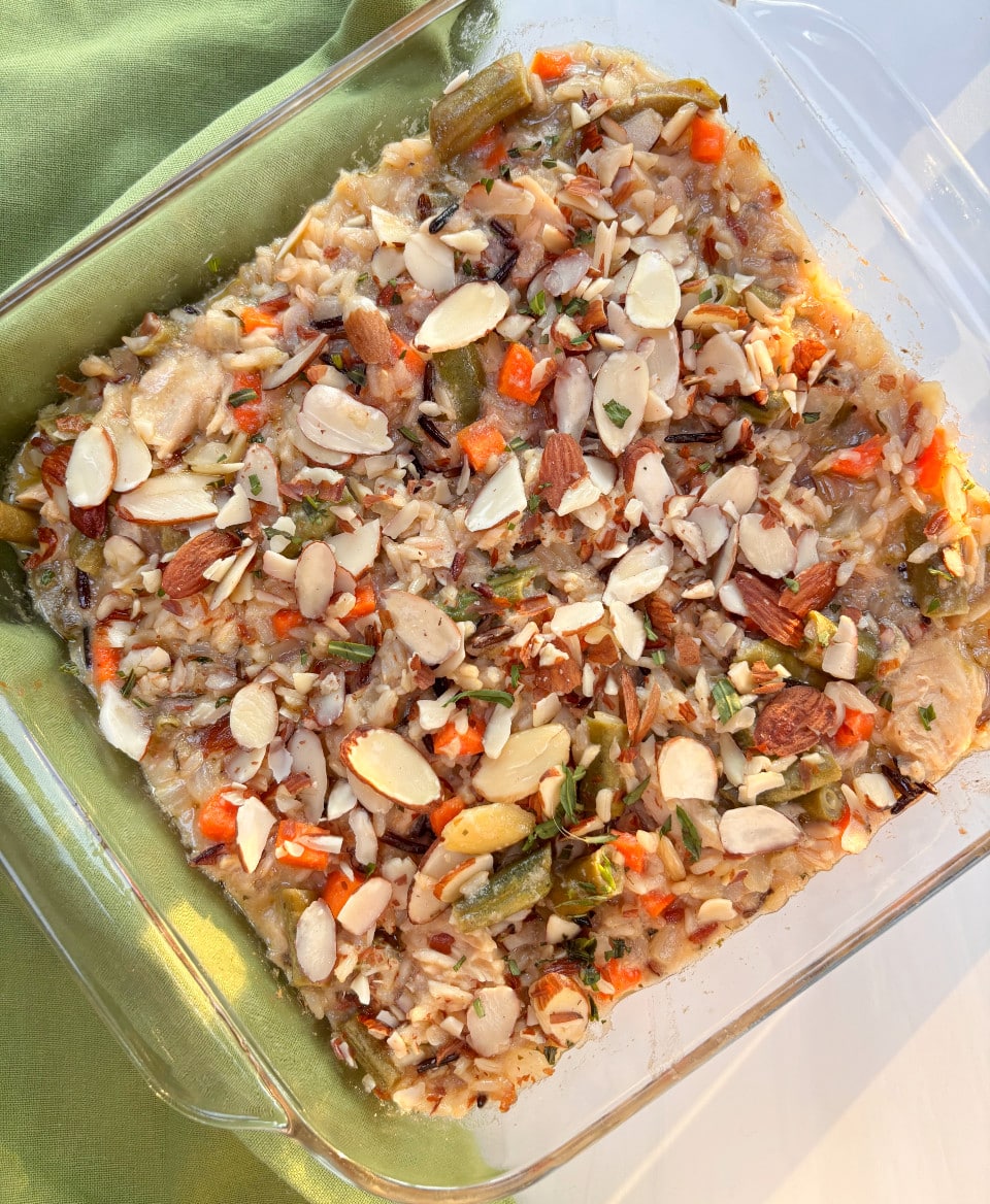 A glass casserole dish filled with salmon and brown and wild rice and vegetables, topped with sliced almonds.