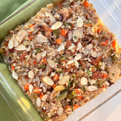 A glass casserole filled with baked salmon and brown and wild rice casserole with almonds on top. A green linen is on the side.