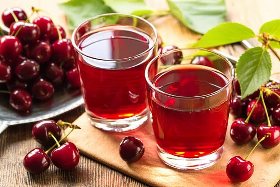 Cherry Juice 2 glasses of cherry juice with fresh cherries in a dish next to them and on the table surrounding them