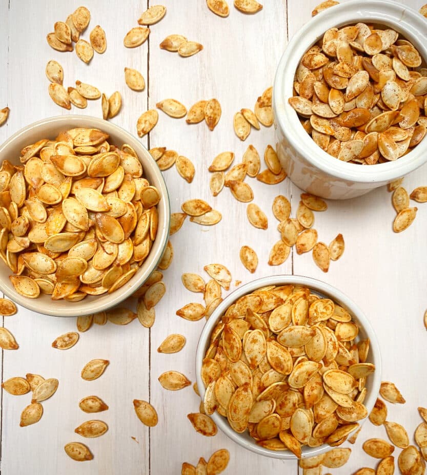 Roasted Pumpkin Seedssleep 3 white bowls filled with roasted pumpkin seeds on a white picnic table