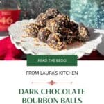 A white platter of chocolate bourbon balls with a red cloth below and bottle of bourbon in the background.