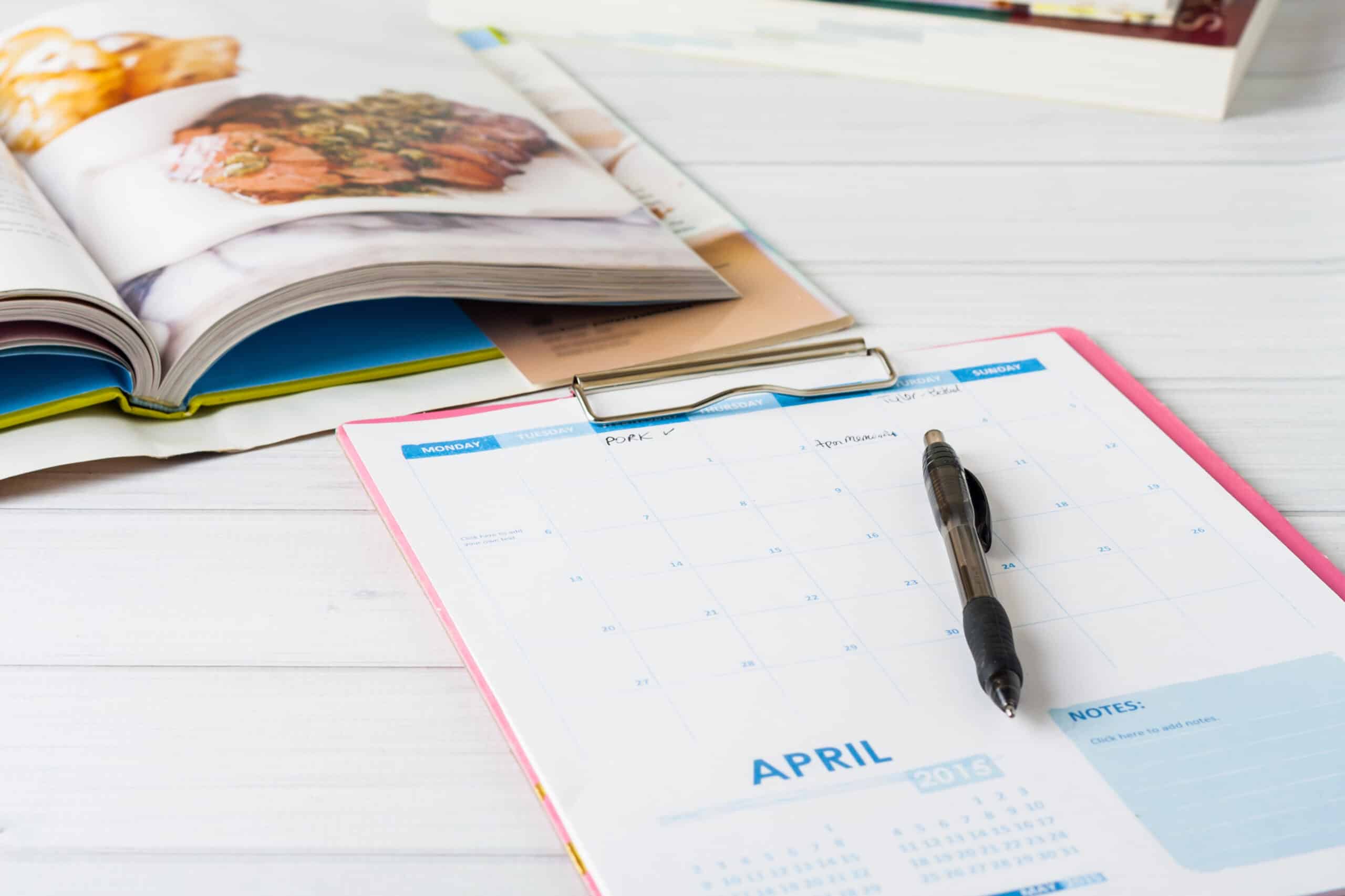 A planner page on a clipboard with a cookbook in the background