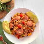 A white bowl filled with Southwestern Turkey Sausage, Rice, and vegetables. Slices of avocado and limes are on the side.