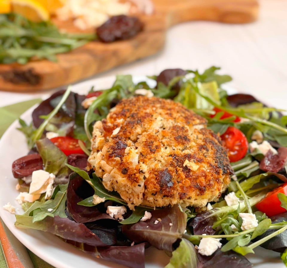 A salmon burger with canned salmon on top of a green salad