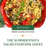 A red bowl filled with tortellini pasta salad with a green linen napkin beside the bowl. The title summer pasta salad everone loves is below