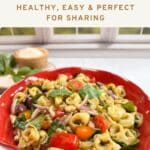 Tortellini pasta and fresh vegetables tossed with pesto in a red bowl