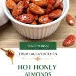 Roasted Honey Coated almonds in a small white bowl on a wood table. The title Hot Honey Almonds: the ultimate salad topper is below