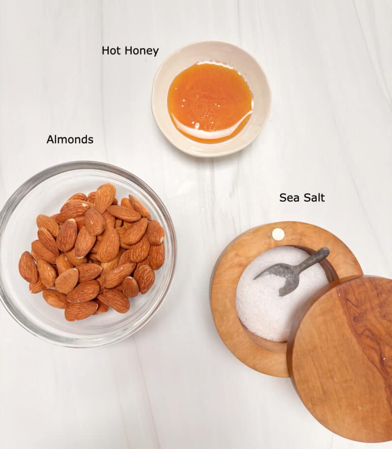Ingredients for Hot Honey Almonds A marble counter with a bowl of almonds, a bowl of honey and some salt