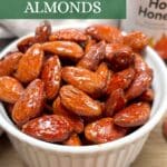 A small white bowl filled with roasted hot honey almonds with a container of hot honey in the background