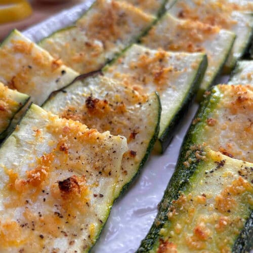 A white platter filled with strips of crispy parmesan coated zucchini