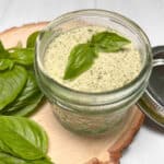 A mason jar with homemade basil salt sitting on a wood board with fresh basil surrounding it.