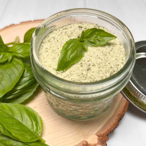 A mason jar with homemade basil salt sitting on a wood board with fresh basil surrounding it.