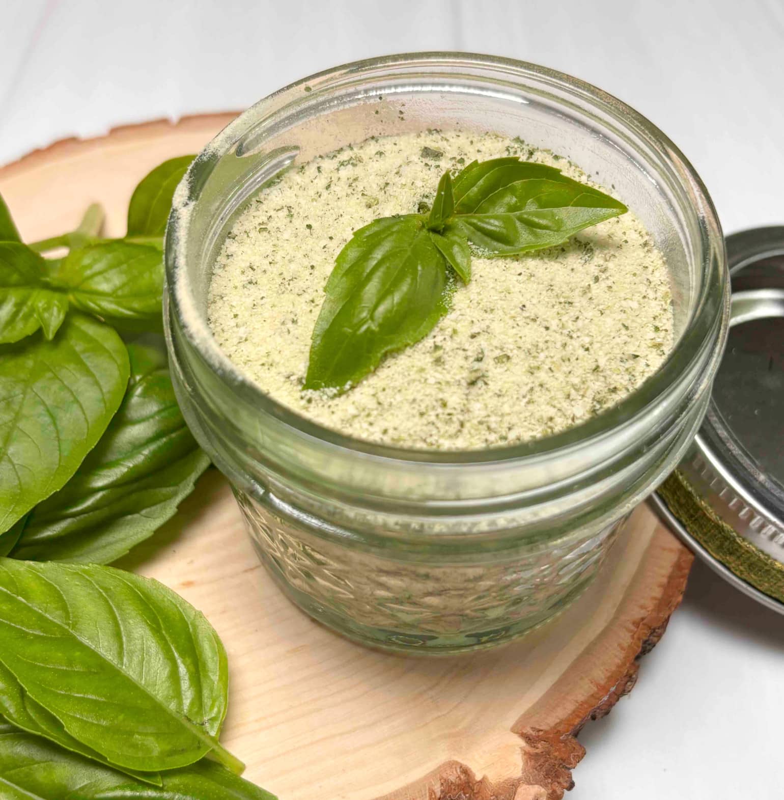 A mason jar with homemade basil salt sitting on a wood board with fresh basil surrounding it.